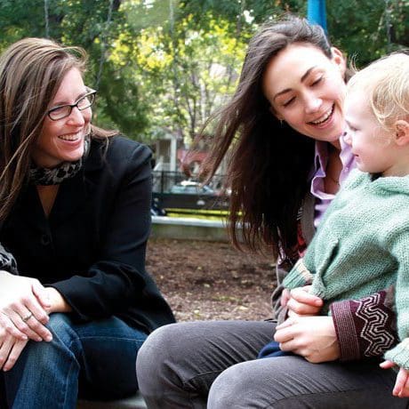 a woman smiling at a child sitting on another woman’s lap