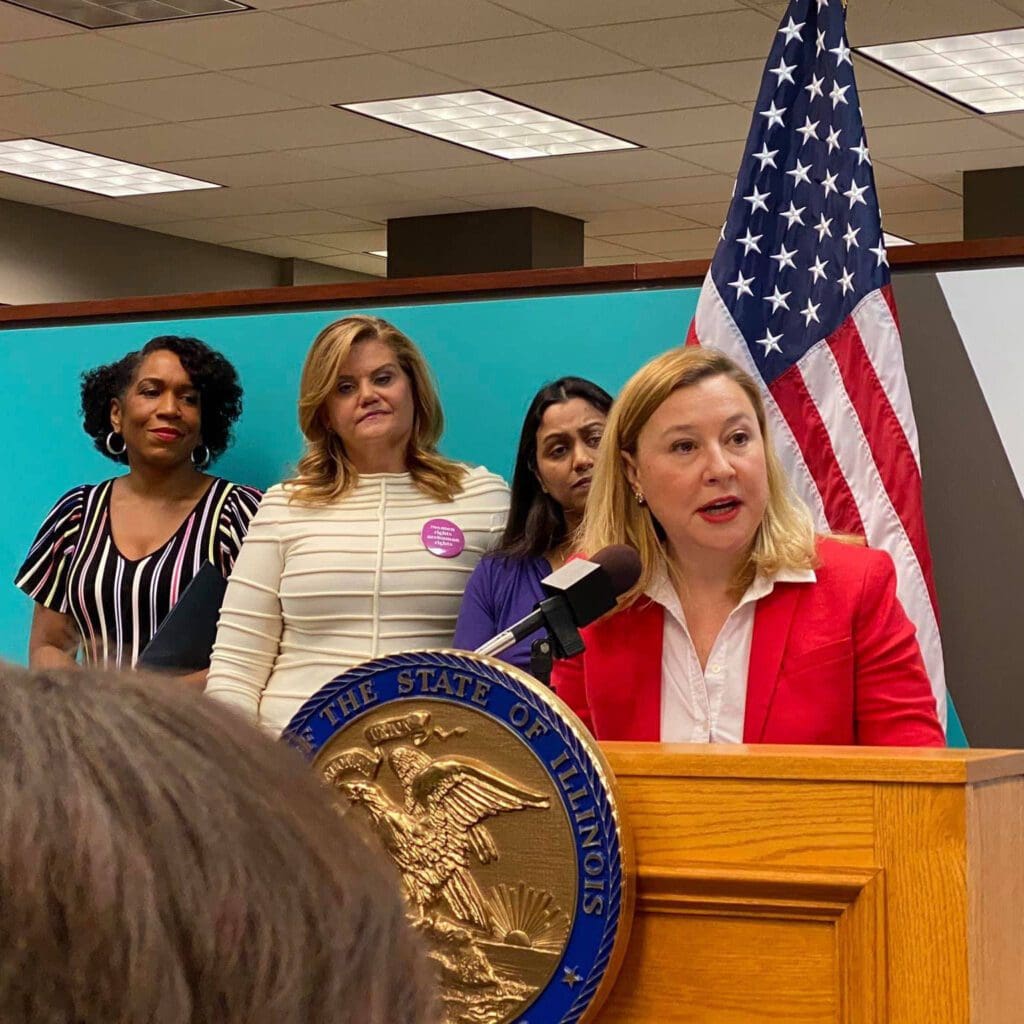  three women behind a woman speaking on a podium