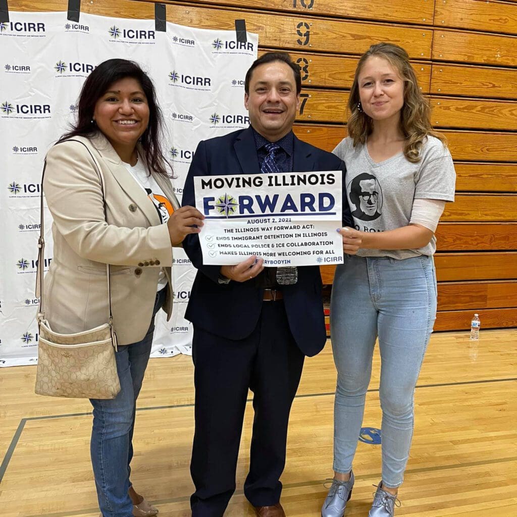 two women beside a man holding a sign saying moving Illinois forward