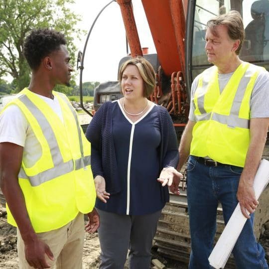  a woman standing in between two men wearing safety vests