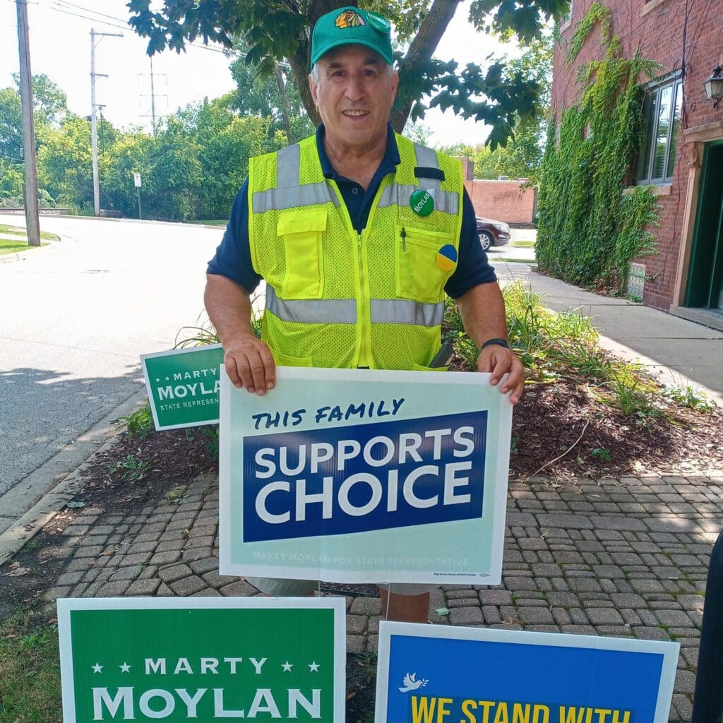 a man wearing a green cap and a safety vest holding a sign that says this family supports choice